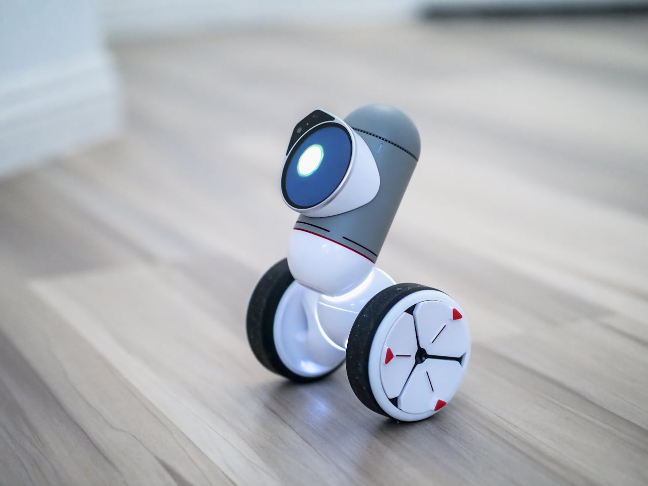Close-up of a modern toy robot with wheels on a wooden floor, emphasizing its design and technology.